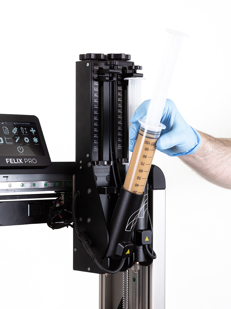 Action shot loading plastic basic syringe into Felix 3D food printer – quick, tool-free cartridge swap